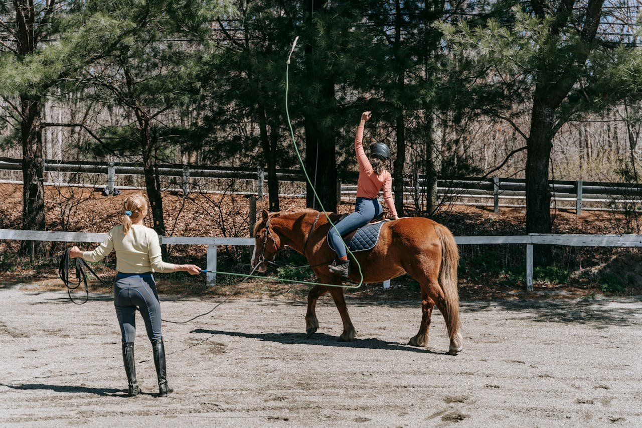 Two people engaged in horse riding training outdoors on a sunny day.