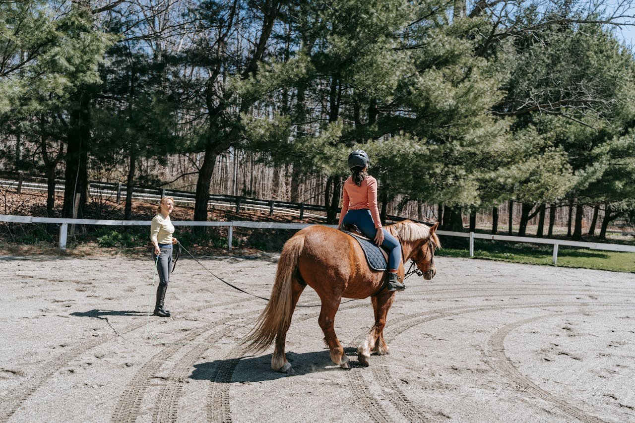 Woman on horseback receiving instruction in outdoor equestrian setting.